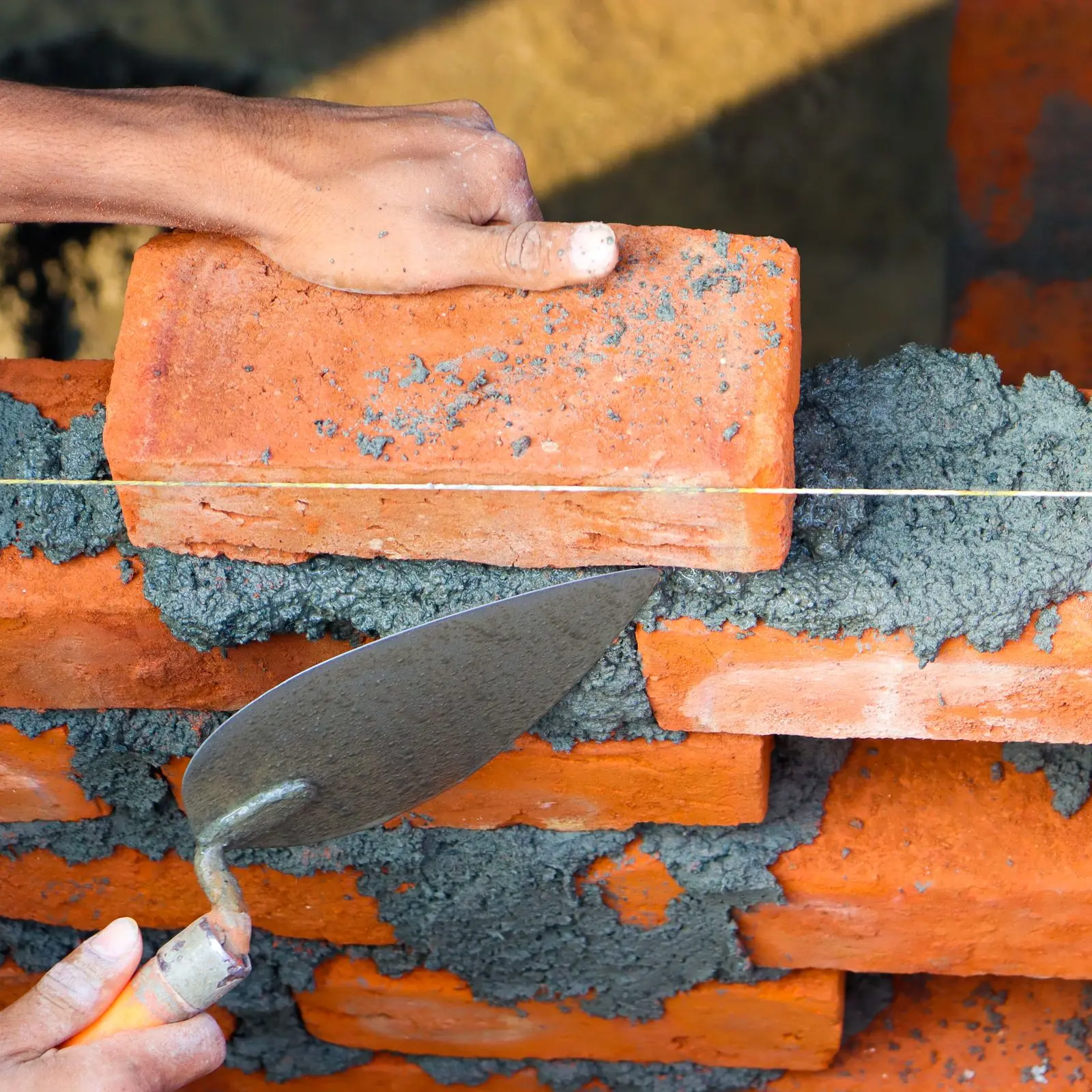 Close-up of hands laying red bricks with mortar and a trowel