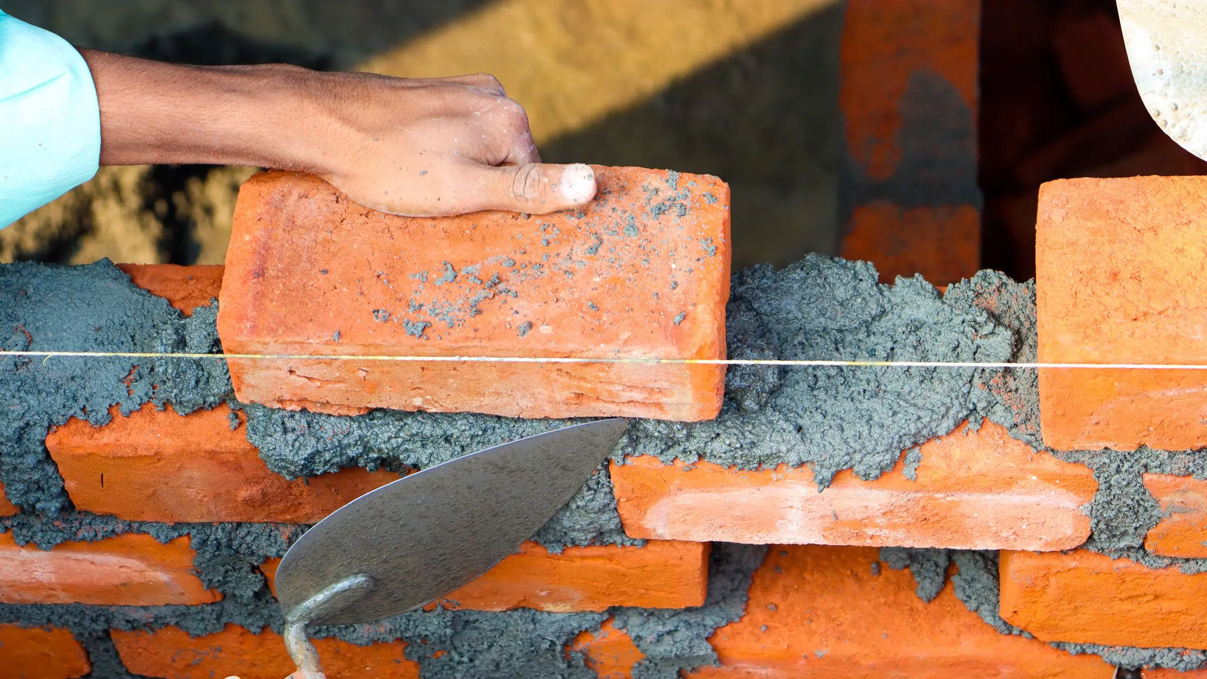 Hands laying red bricks with mortar and a trowel