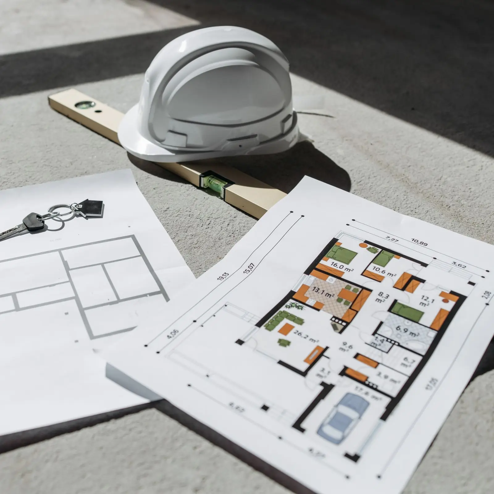 Floor plans, a white safety helmet and a spirit level on a concrete floor
